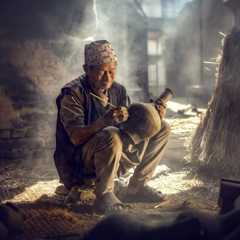 The old man is painting in a clay pot in Durbar square near old hindu temples.